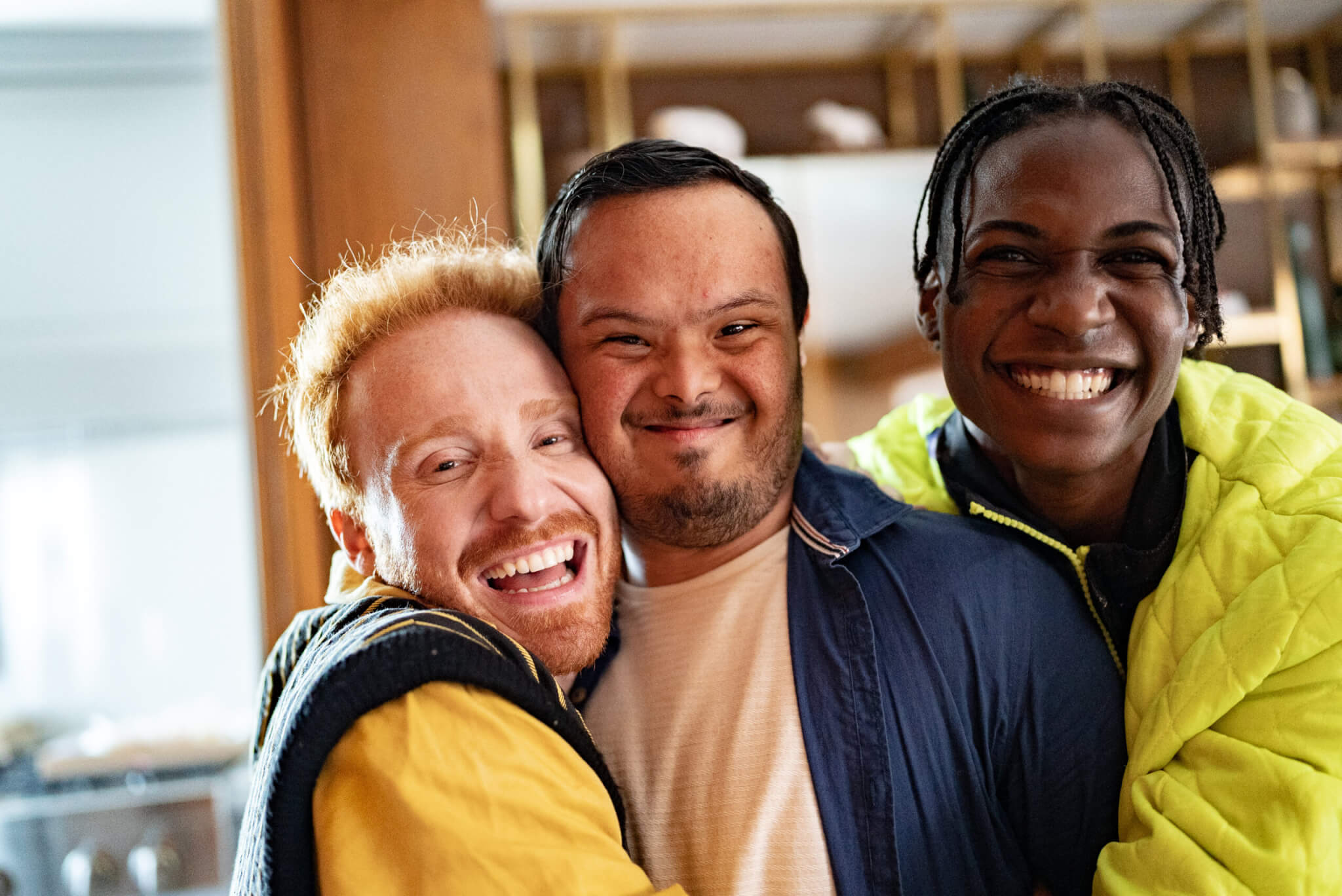 drei junge Männer umarmen sich. Sie haben unterschiedliche Hautfarben, manche haben Behinderungen.